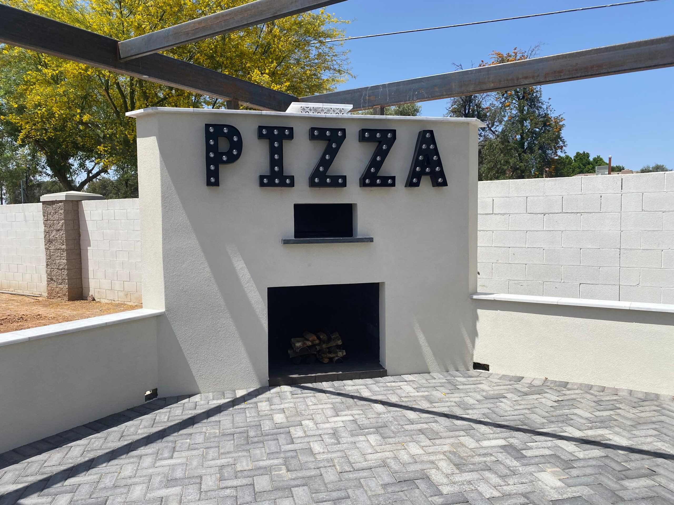 A pizza oven in a backyard with a sign that says pizza.